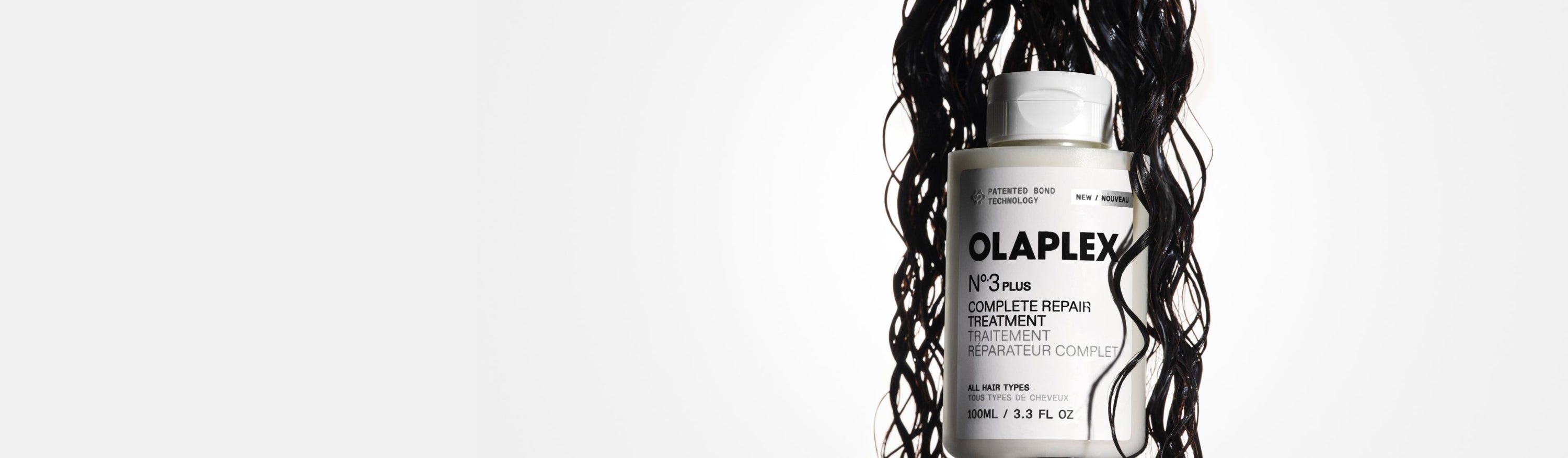 Wet, curly dark hair hanging down and encompassing a No.3PLUS bottle