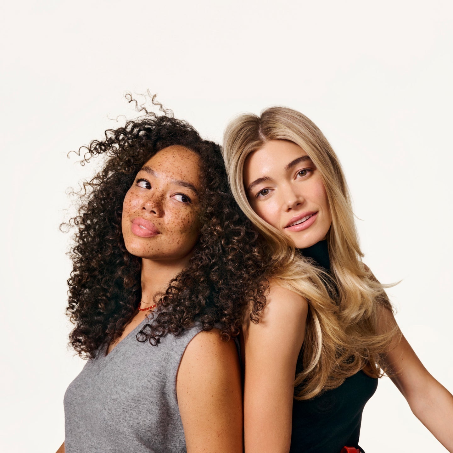Two women leaning against each other, one with straight blonde hair and the other with curly brunette hair