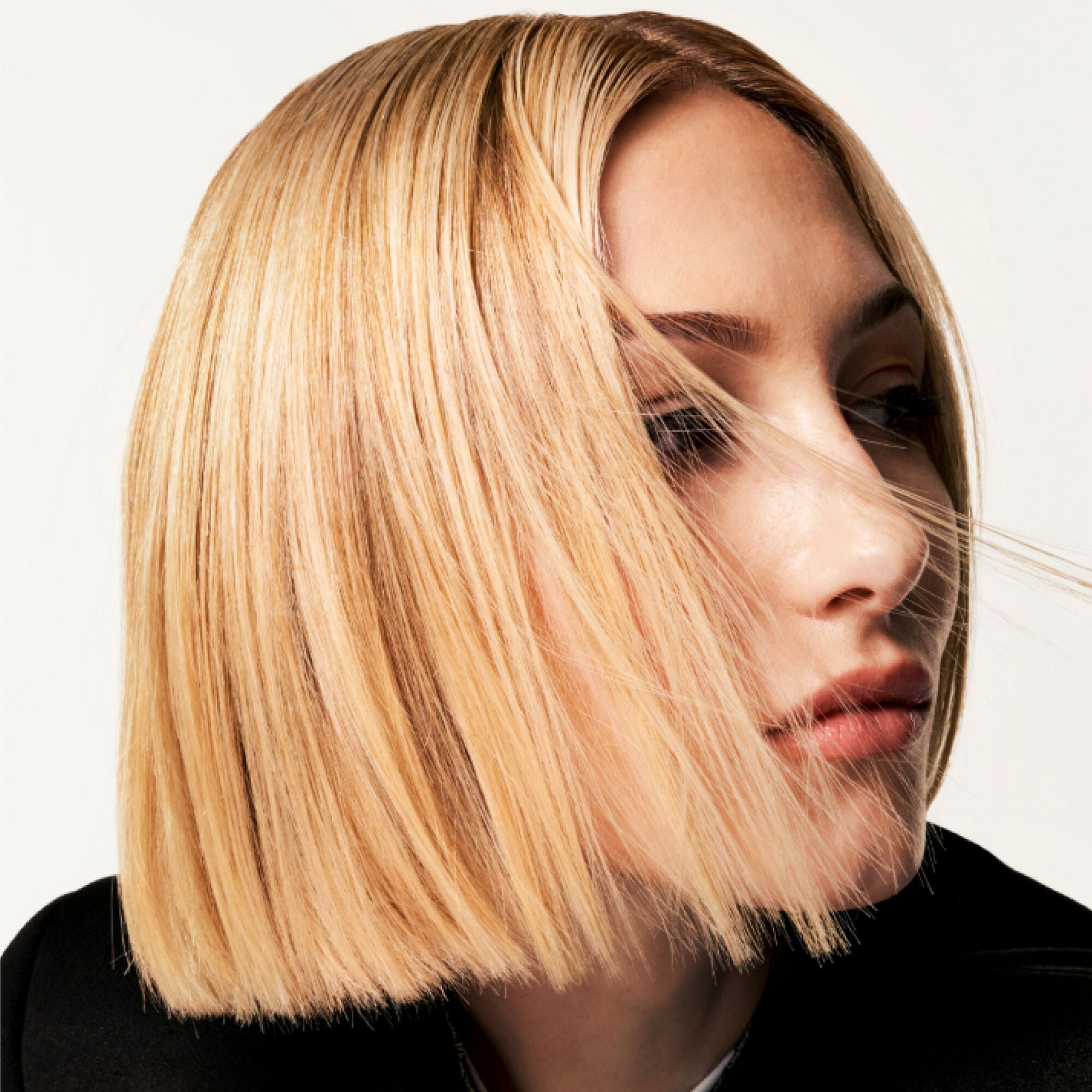 Donna con un elegante taglio di capelli biondo a caschetto su uno sfondo neutro