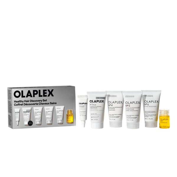 Un'immagine prodotto del set Healthy Hair Discovery di Olaplex su uno sfondo trasparente a scacchiera. A sinistra c'è la scatola del prodotto, e a destra sono disposti cinque tubi bianchi di dimensioni da viaggio (N°.3, N°.4, N°.5, N°.6, e un tubo più piccolo) accanto a una piccola bottiglia trasparente di Bonding Oil N°.7 riempita di liquido giallo. - main view