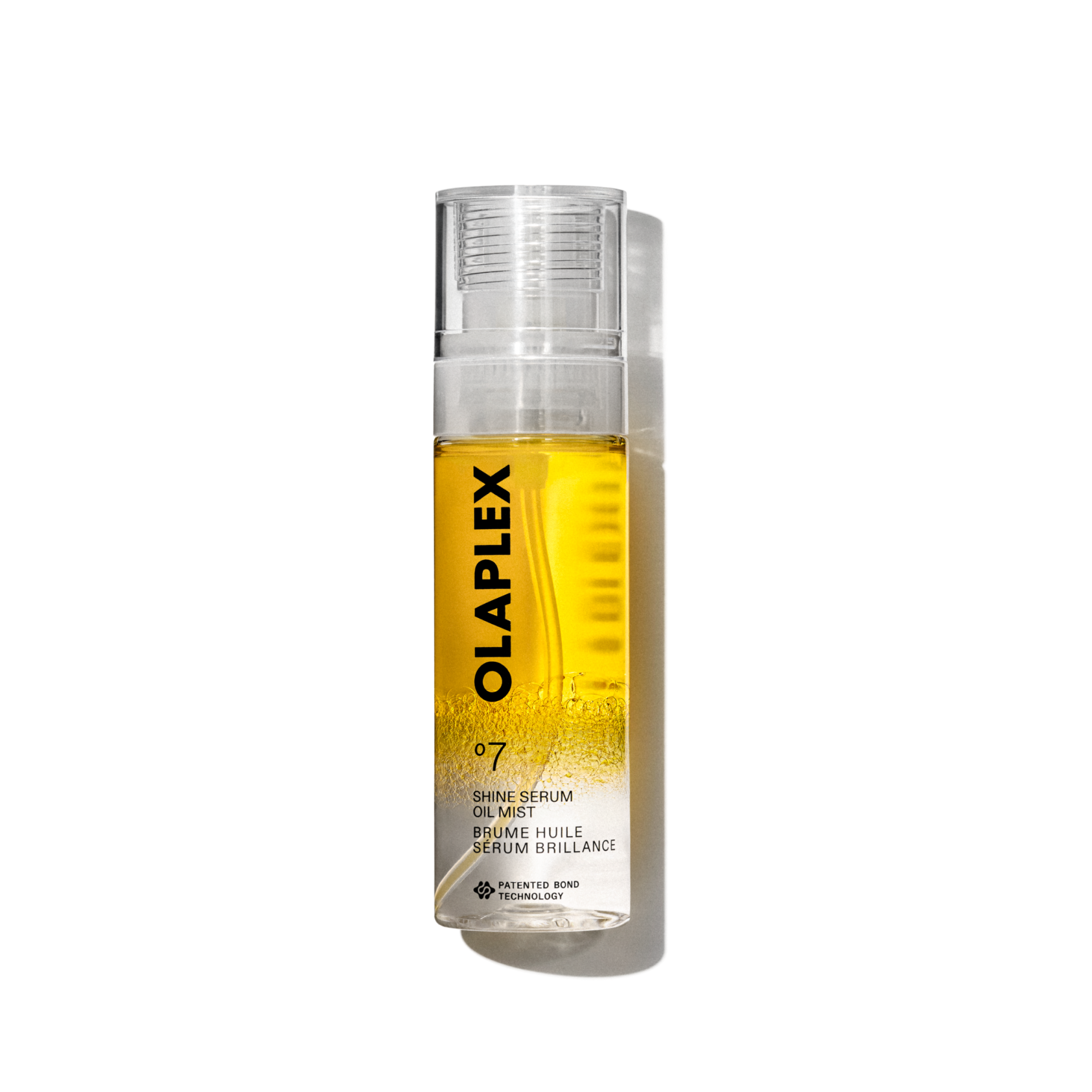 Una foto del prodotto Olaplex No. 7 Shine Serum Oil Mist in un flacone spray trasparente da 80 ml. Il flacone presenta un liquido giallo brillante visibile all'interno, un tappo trasparente e un'etichetta bianca pulita nella parte inferiore con testo nero che riporta il nome del prodotto, i dettagli e il caratteristico logo "No. 7". Il flacone è isolato su uno sfondo trasparente a griglia.