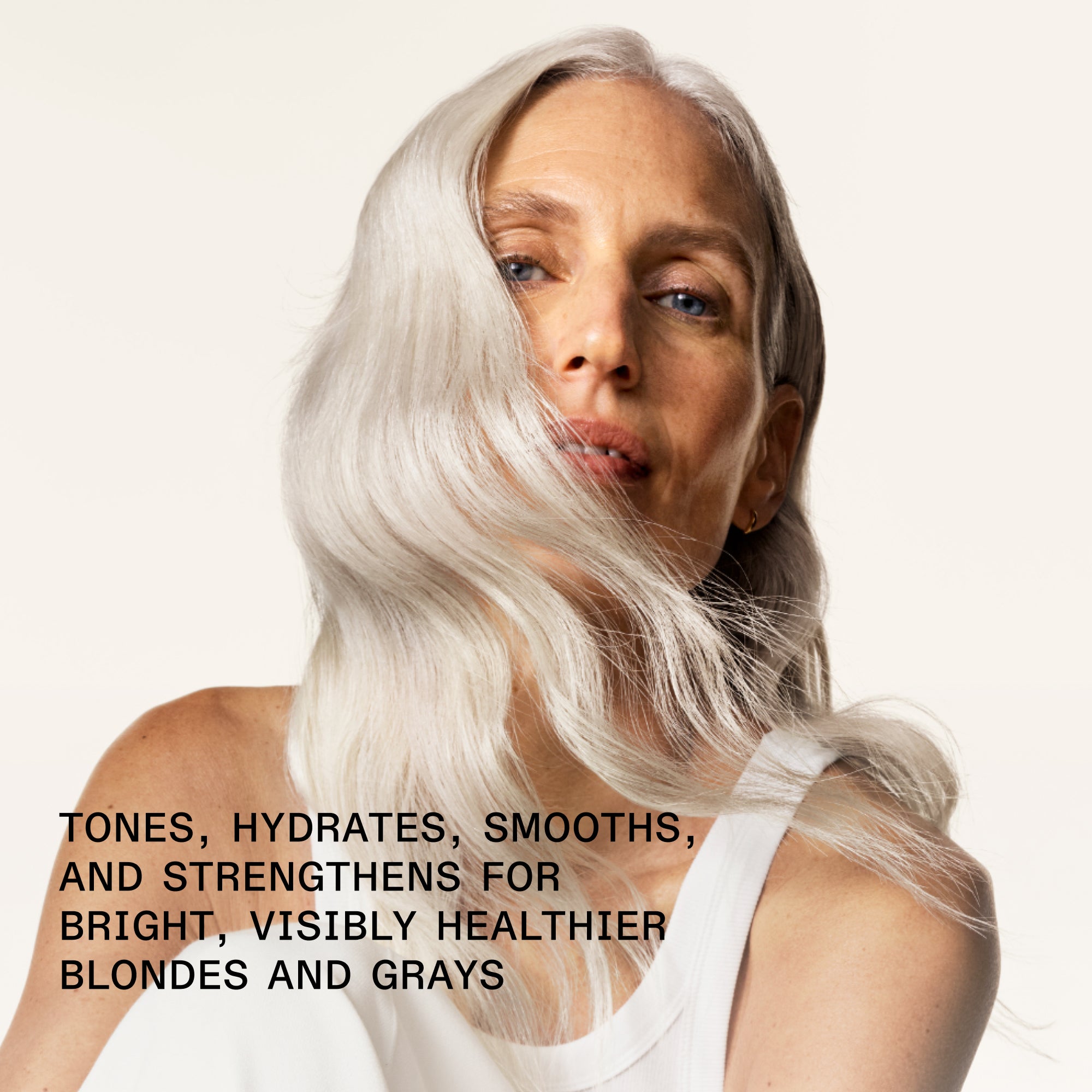 A close-up profile view of a woman with long, flowing, light platinum blonde hair blowing across her face. Bold black text in the bottom left corner reads: "TONES, HYDRATES, SMOOTHS, AND STRENGTHENS FOR BRIGHT, VISIBLY HEALTHIER BLONDES AND GRAYS."