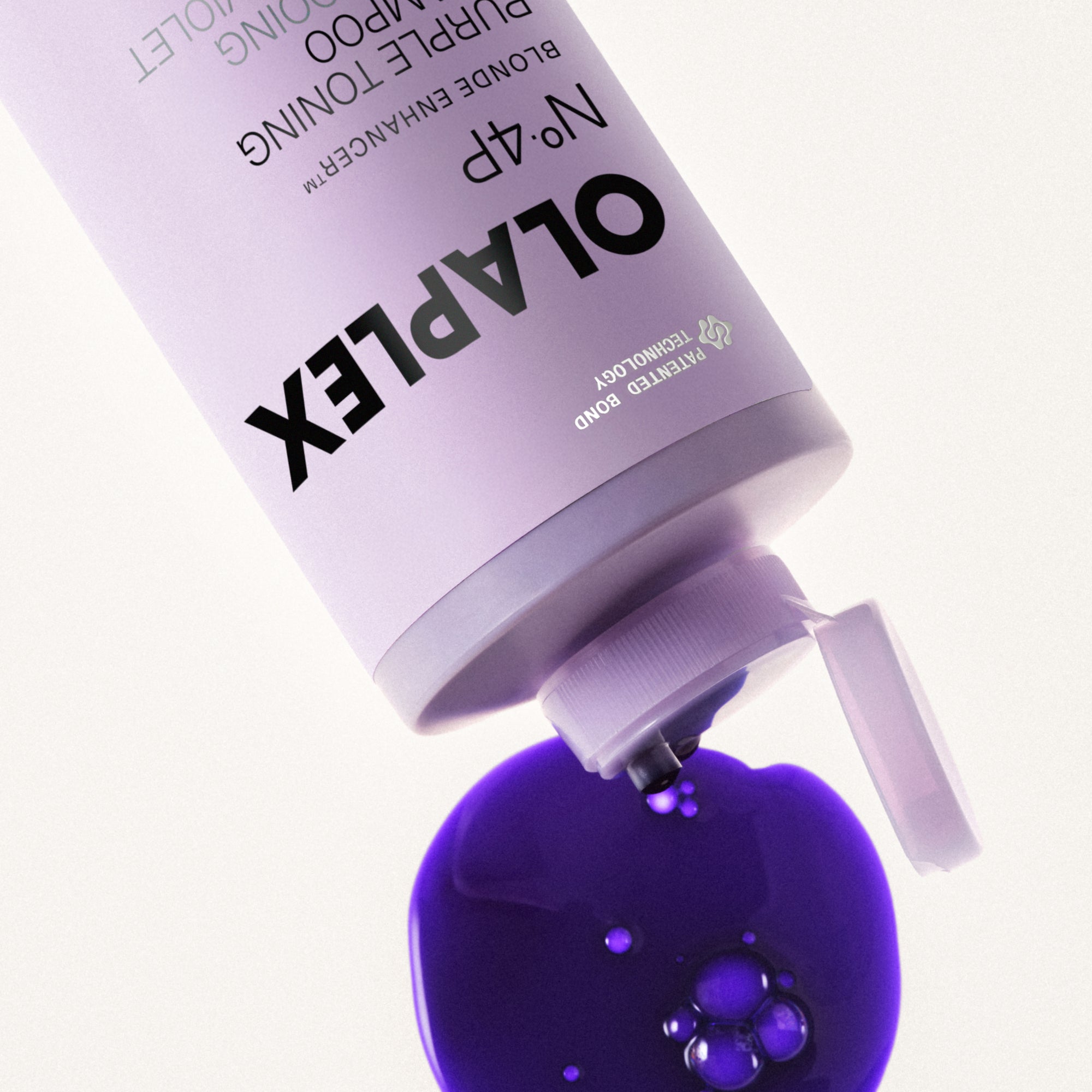 An up-close view of a light purple Olaplex bottle tilted downward, dispensing a glossy, thick puddle of vibrant purple toning shampoo with tiny air bubbles onto a clean white background.