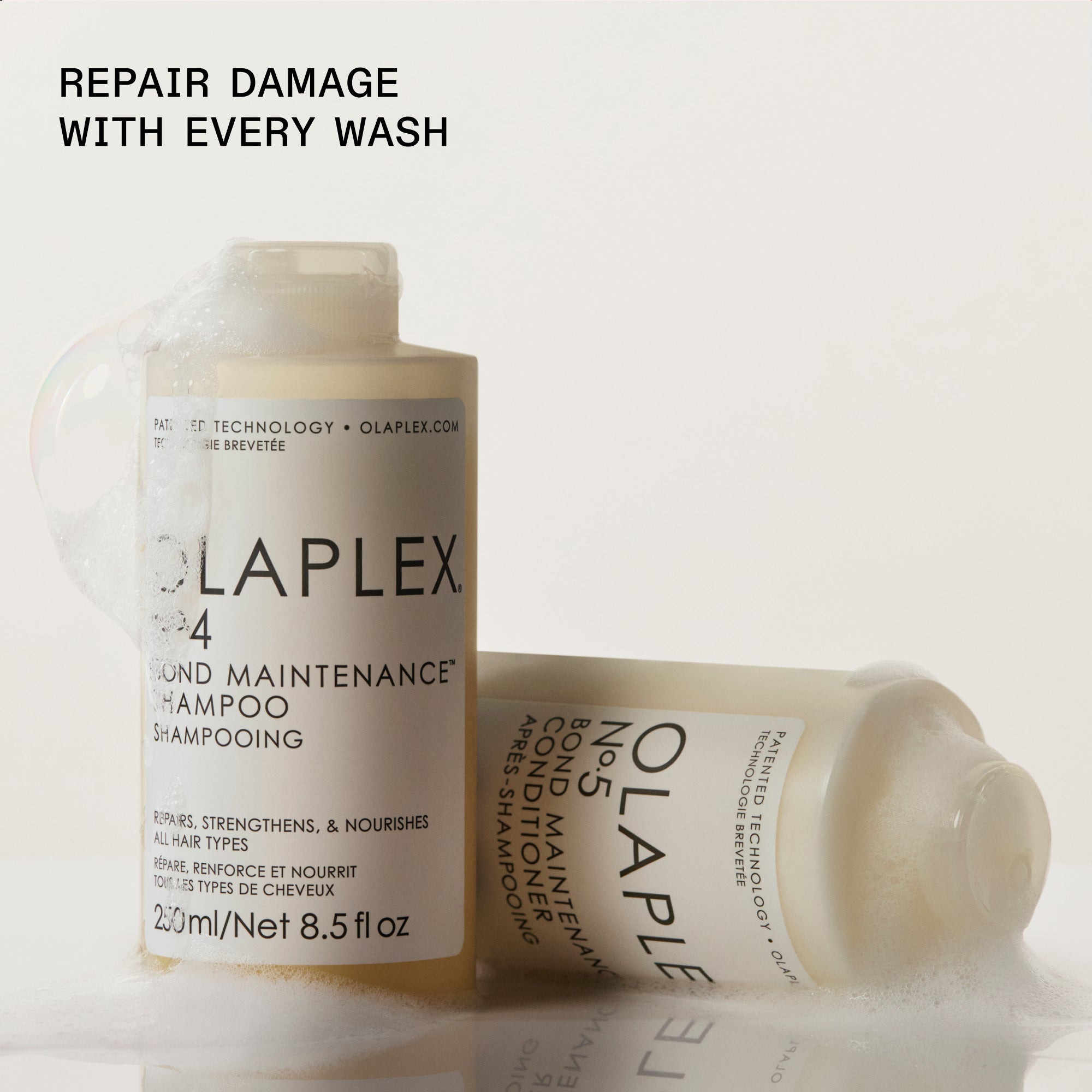 Bottiglie di shampoo e balsamo Olaplex posizionate su uno sfondo chiaro. A sinistra è visibile una bottiglia di "OLAPLEX N°.4 BOND MAINTENANCE SHAMPOO" in posizione verticale, mentre a destra una bottiglia di "OLAPLEX N°.5 BOND MAINTENANCE CONDITIONER" è appoggiata orizzontalmente su un lato. Il testo nero in grassetto nell'angolo in alto a sinistra recita: "RIPARA I DANNI AD OGNI LAVAGGIO".